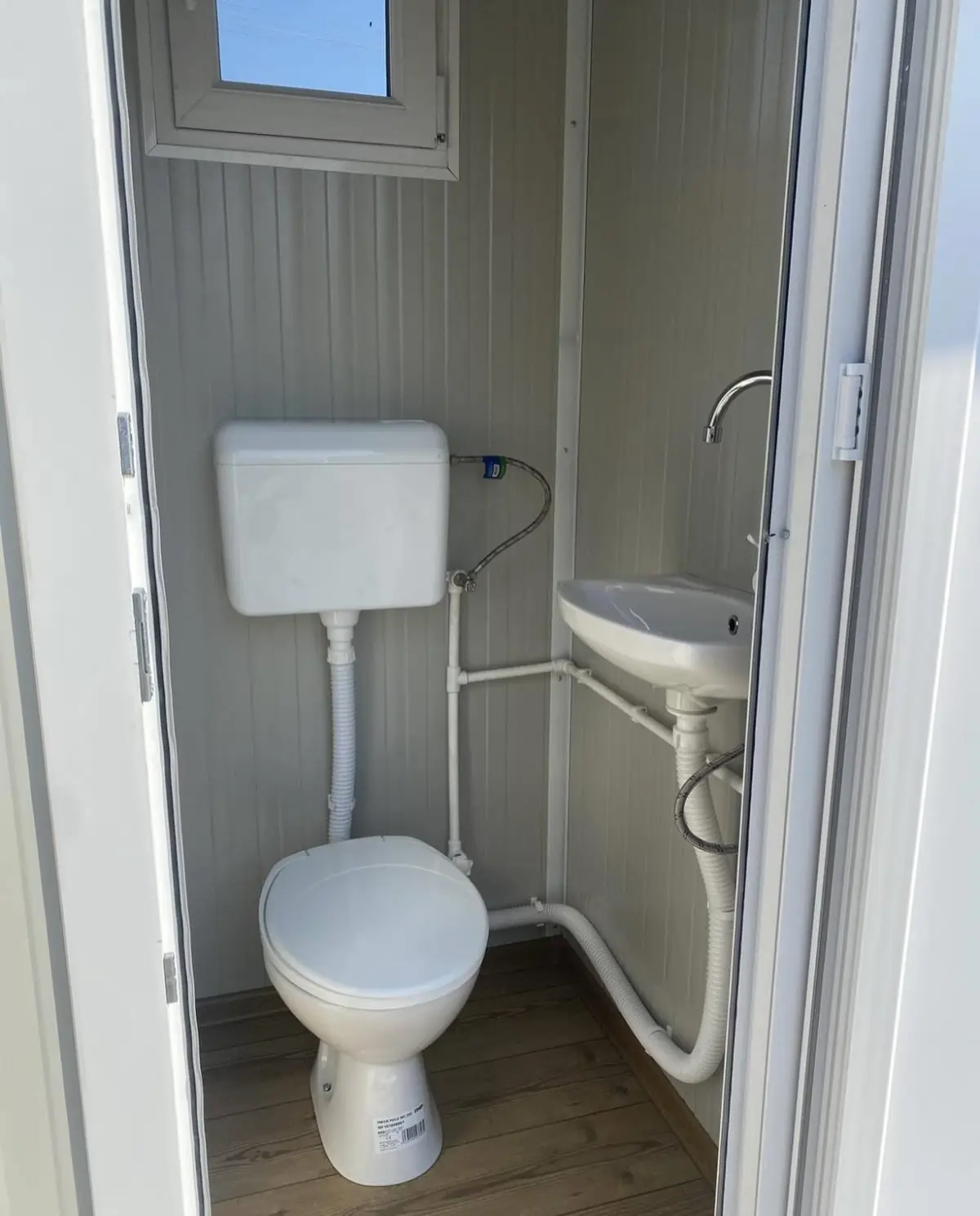 Inside a flushing restroom cabin with a white toilet, tank and small sink