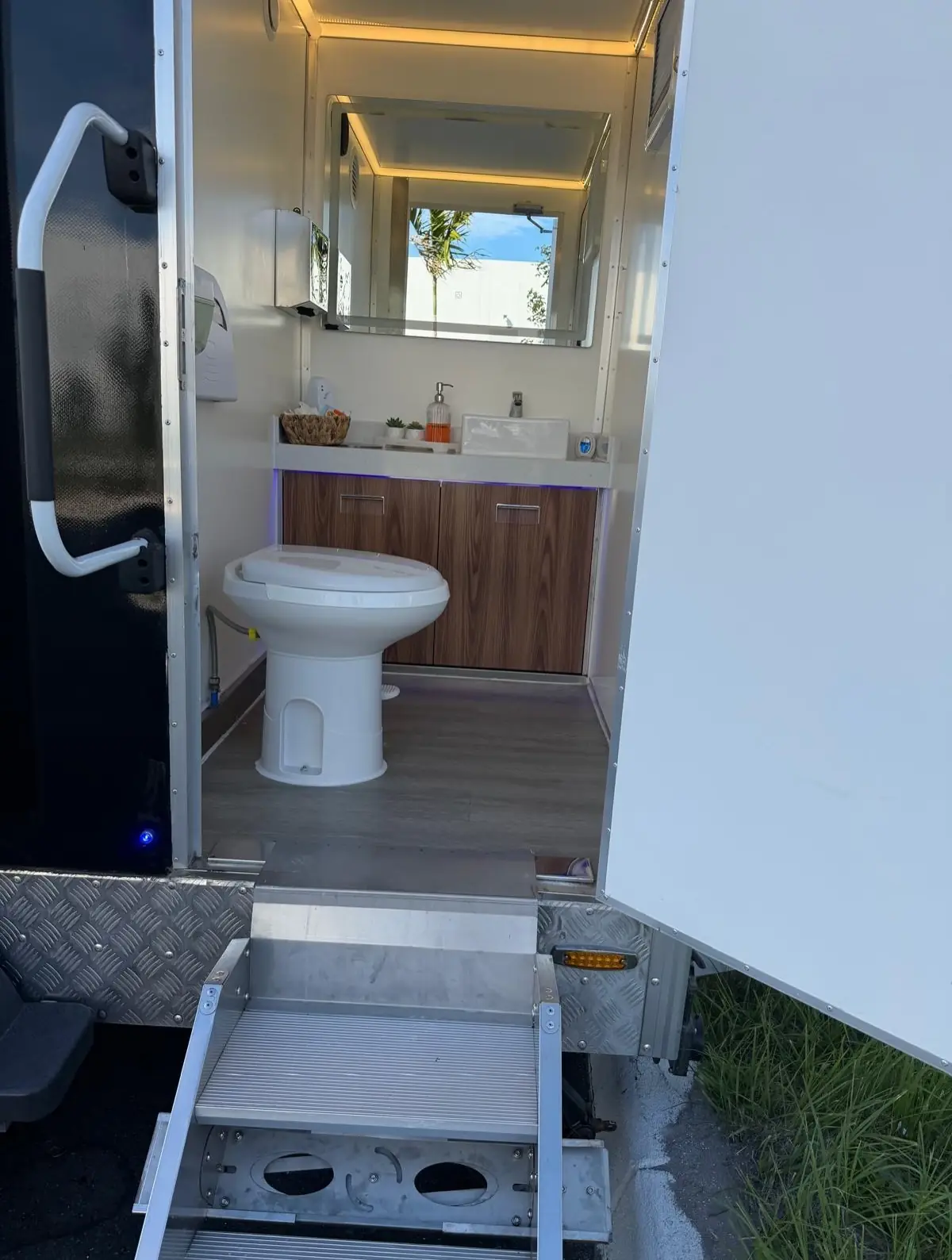 Restroom trailer stall with a toilet and wood vanity