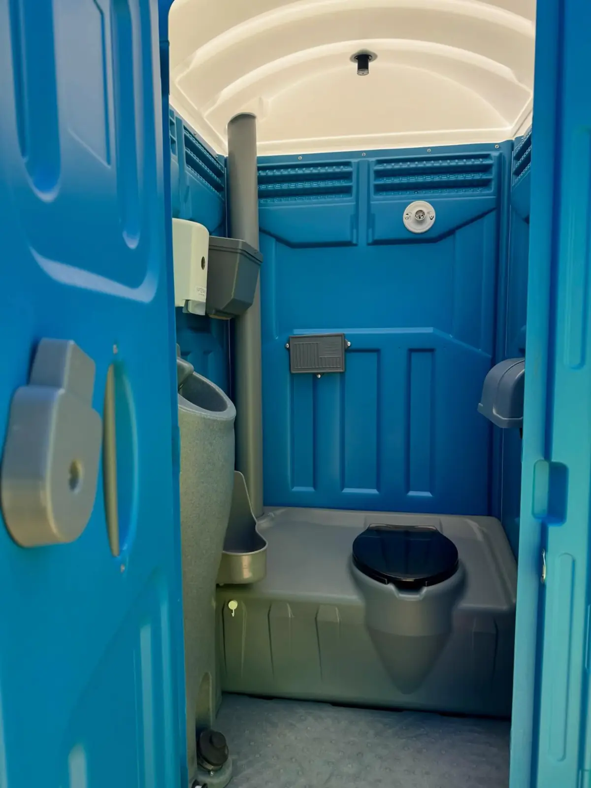 Inside a blue standard porta potty showing the seat and wall urinal